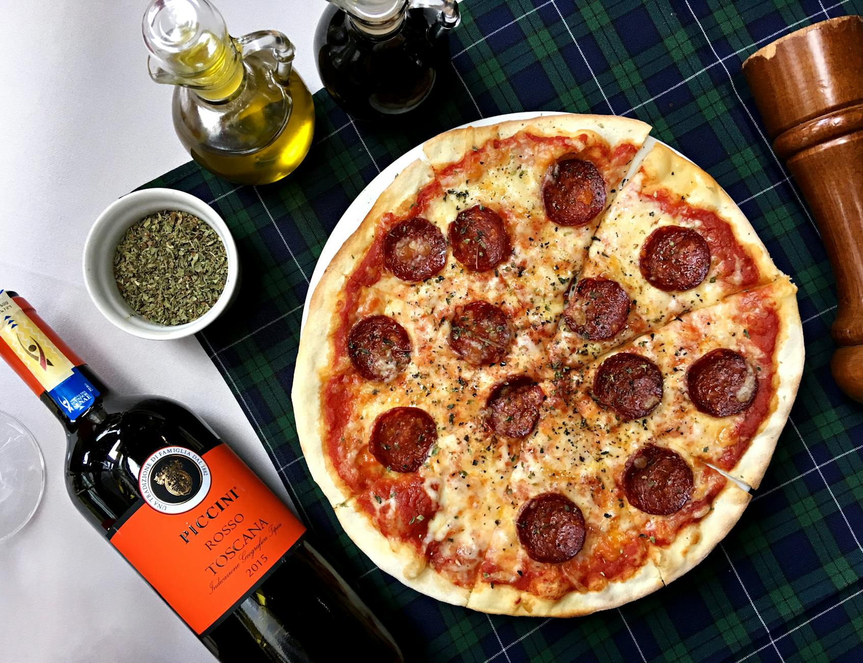 Pizza pepperoni i kieliszek czerwonego wina na kraciastym obrusie